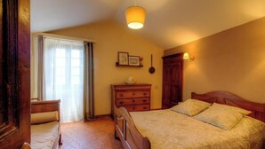Een slaapkamer met een bed, een dressoir, een nachtkastje, een lamp en een raam met gordijnen.