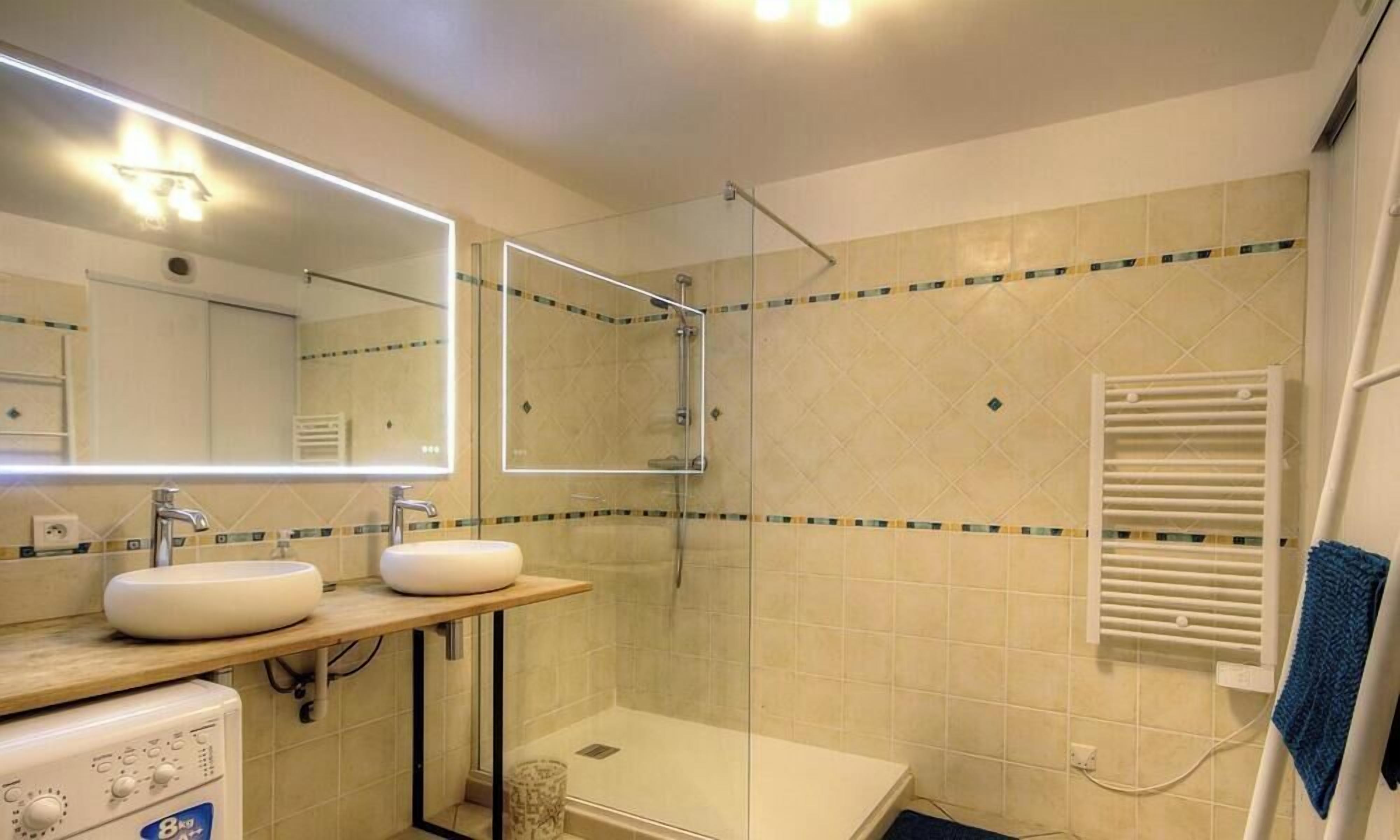 A bathroom with a glass-enclosed shower, two sinks, a mirror, and a towel rack.