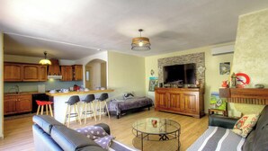 A cozy living room with a sofa, a coffee table, and a TV. There's a kitchen area with wooden cabinets and a dining table with stools. - Le 55742 - LUCCIANA - Gîte (LUCCIANA)