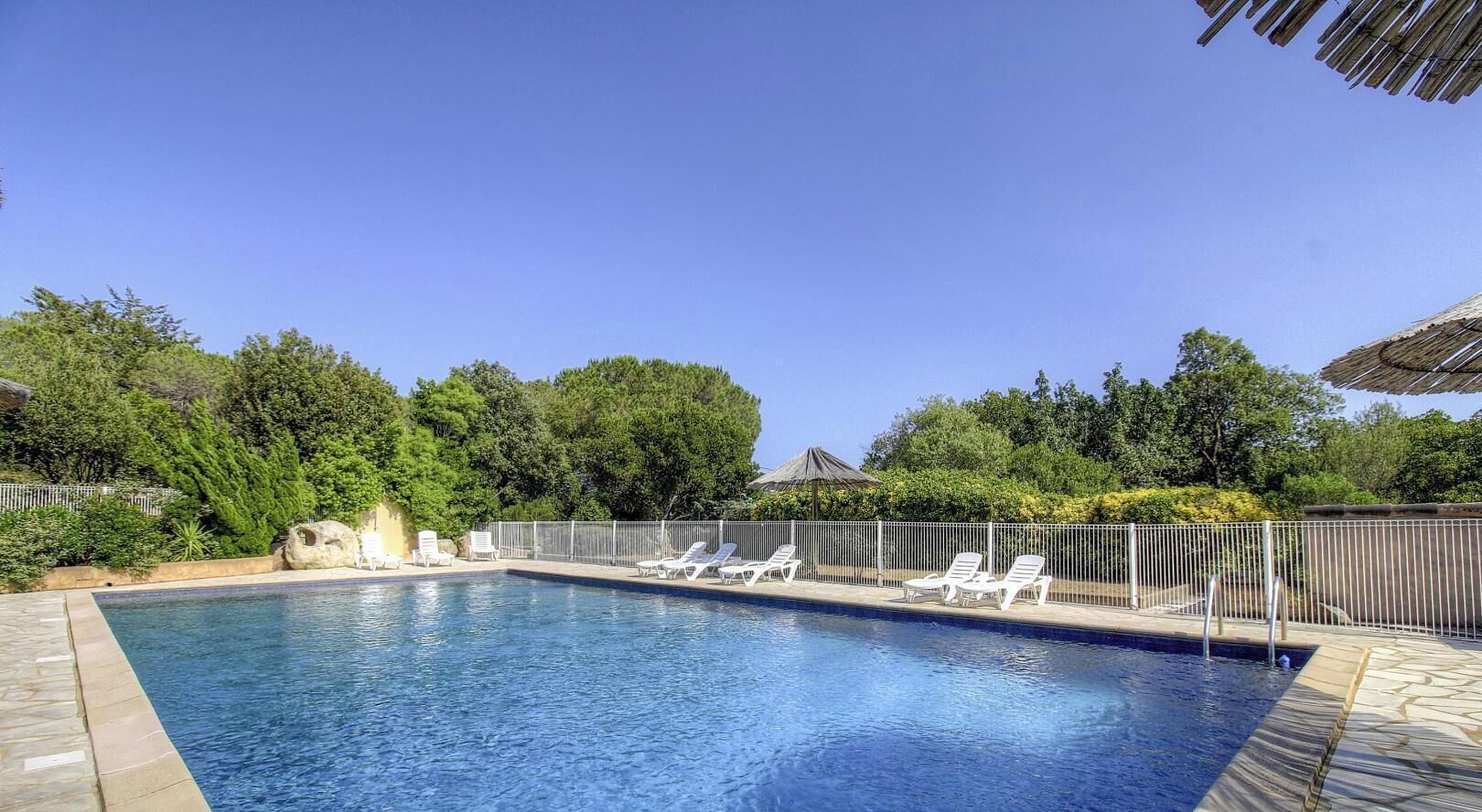 Ein Swimmingpool mit Liegestühlen, umgeben von einem Zaun und Bäumen.