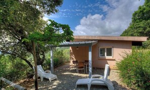 Ein eingeschossiges Gebäude mit Terrasse, Sitzgelegenheit im Freien und einer Pergola.