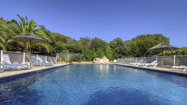 Ein Swimmingpool mit Liegestühlen und Sonnenschirmen, umgeben von viel Grün.