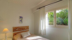 Ein Schlafzimmer mit Bett, Nachttisch, Lampe, einem Fenster mit Vorhängen und einem Bild an der Wand.