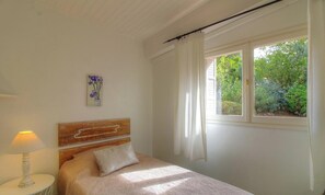Ein Schlafzimmer mit Bett, Nachttisch, Lampe, einem Fenster mit Vorhängen und einem Bild an der Wand.