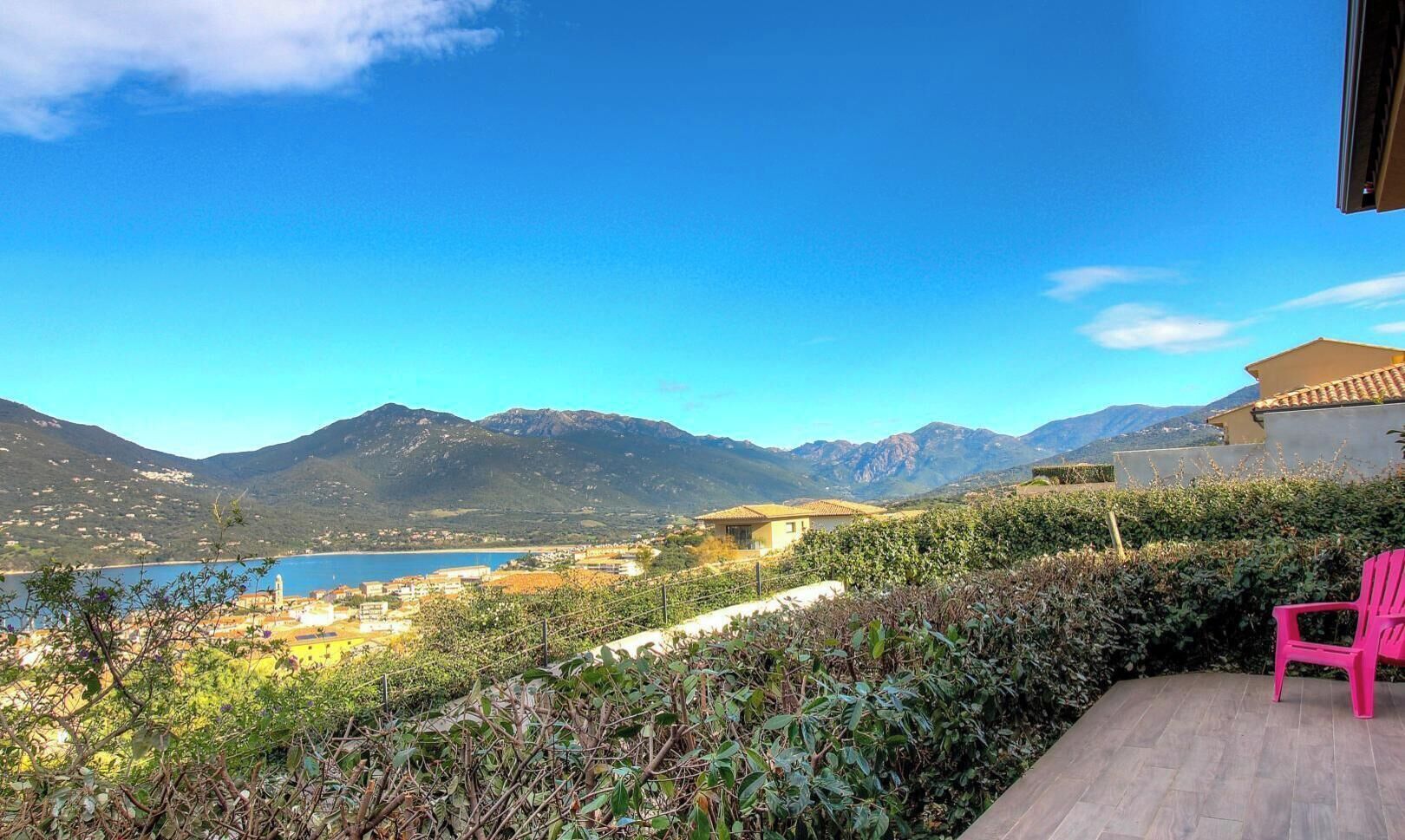 Une vue panoramique d’une région côtière, avec des montagnes, une étendue d’eau et un bâtiment doté d’une terrasse.