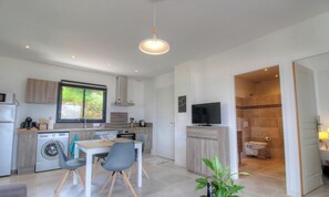 Eine kompakte Küche mit Waschmaschine, ein Essbereich mit Tisch und Stühlen, ein Fernseher auf einem Schrank und ein Badezimmer mit Toilette und Dusche.