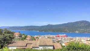Una cittadina costiera con una nave rossa, edifici con tetti in terracotta e una montagna sullo sfondo.