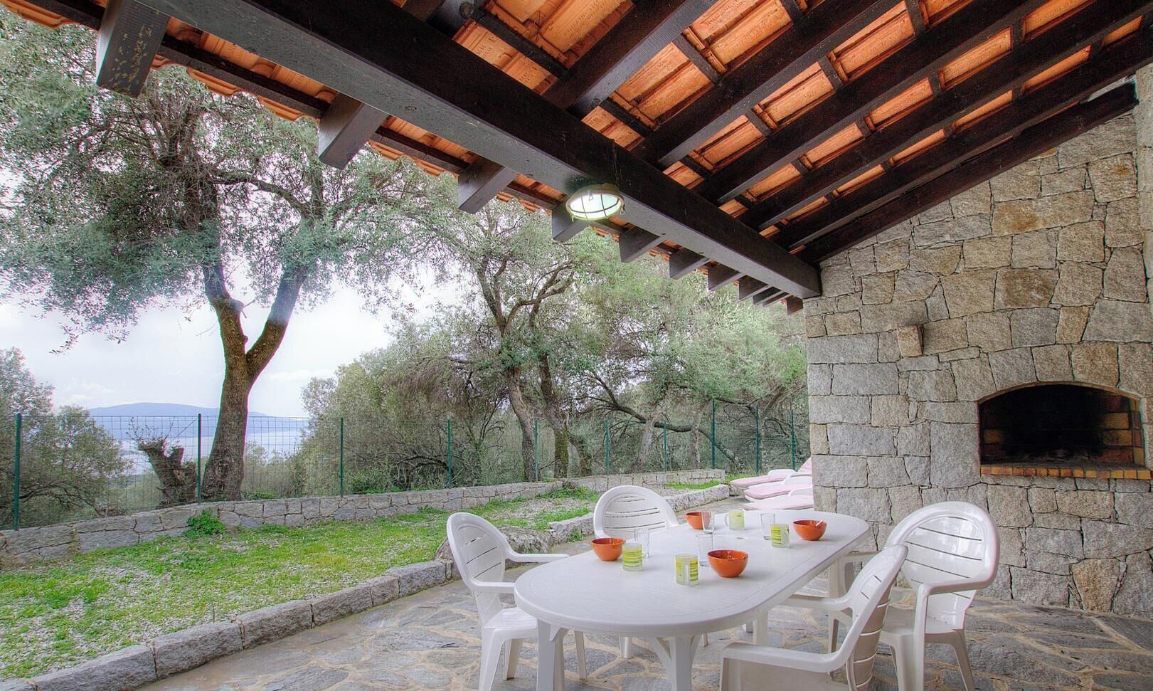 An outdoor patio with a stone wall, a wooden ceiling, and a table set for dining.
