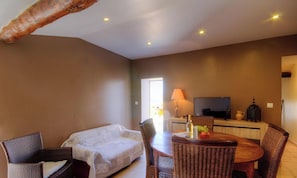 Ein Zimmer mit einer Couch, Stühlen, einem Esstisch, einem Fernseher und einer Lampe.