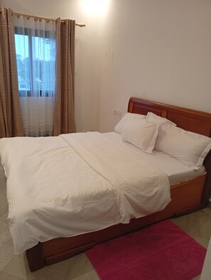 Una cama con sábanas blancas, cabecera de madera y alfombra roja.