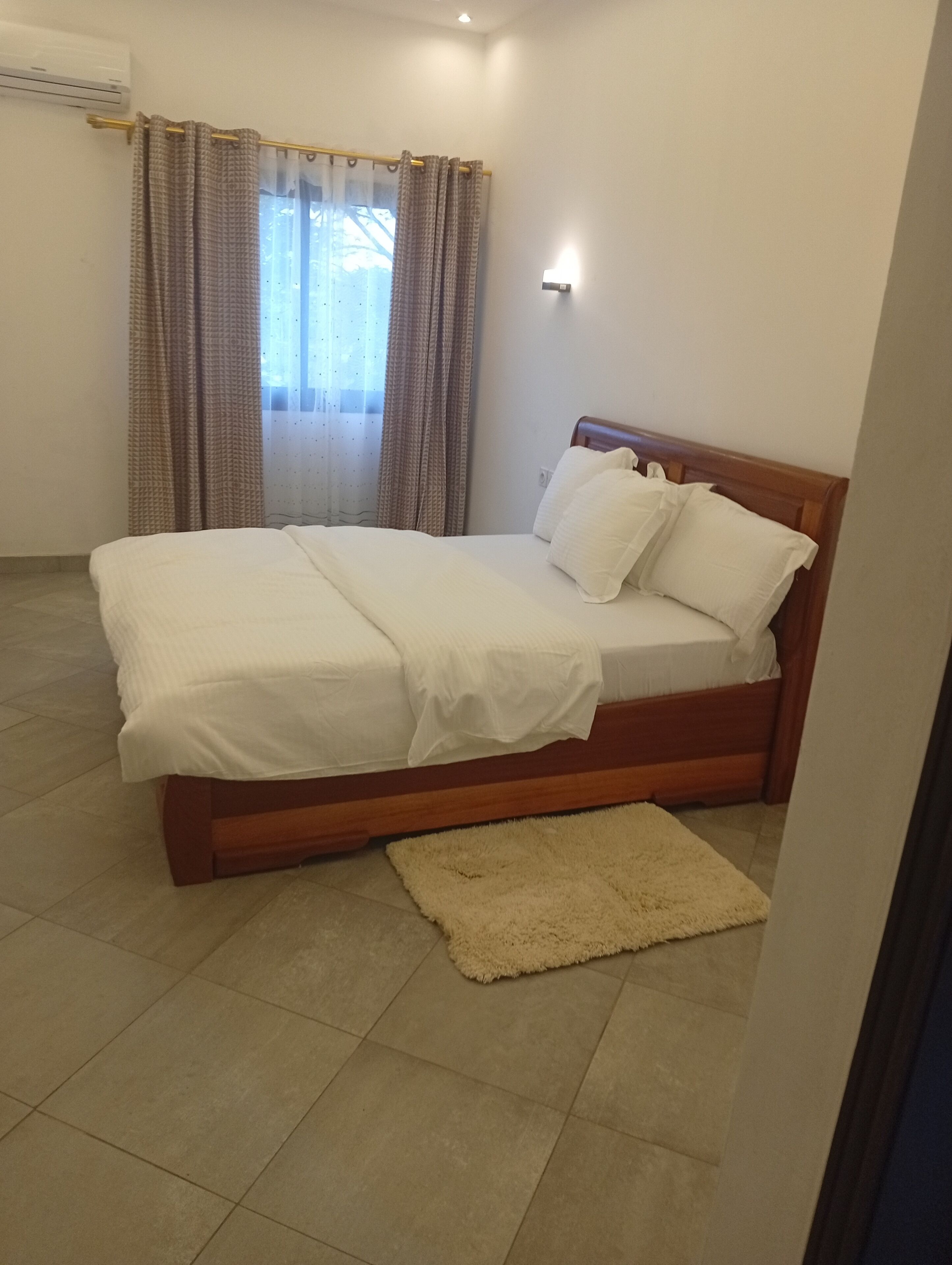 Une chambre à coucher avec un lit, des rideaux, une lampe fixée au mur et un tapis.