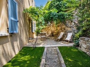 Een stenen muur, een kleine tuin met gras en grind, en tuinmeubilair.