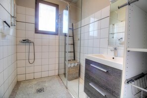 Een badkamer met een douchecabine van glas, een wastafel met spiegel, betegelde wanden en een raam.