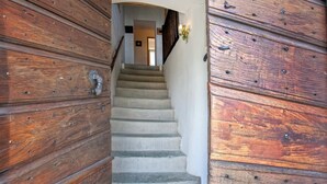 Eine Holztreppe führt zu einem Raum mit weißer Wand und einer Lampe.