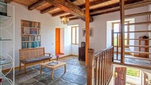 Ein geräumiges Zimmer mit Steinfußboden, Holzmöbeln, einem Bücherregal und einer Treppe.