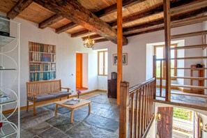 A spacious room with a stone floor, wooden furniture, a bookshelf, and a staircase. - Le 59212 - CAMPILE - Gîte (CAMPILE)