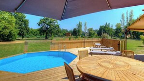 Una piscina con muelle de madera, sillas de descanso y un porche cubierto.