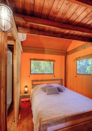 Un dormitorio de cabaña de madera con una cama, una mesita de noche, una lámpara y una ventana.