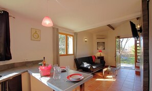 A living room with a sofa, a dining table with plates and glasses, a lamp, and a window. - Le Lilas - SOTTA - Gîte (SOTTA)