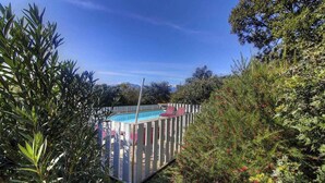 En swimmingpool omgivet af et træhegn, med frodig vegetation og træer i baggrunden.