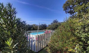 A swimming pool surrounded by a wooden fence, with lush greenery and trees in the background. - Le Lilas - SOTTA - Gîte (SOTTA)