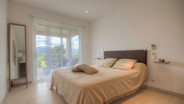 Ein Schlafzimmer mit einem großen Bett, einem Spiegel, einem Nachttisch und Blick ins Freie.