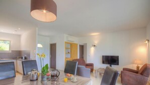 Ein modernes Wohnzimmer mit Essbereich, einem Fernseher und einer Küche im Hintergrund.