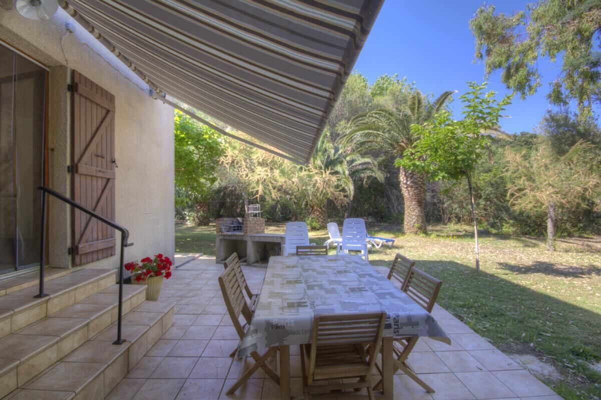 Une terrasse couverte avec une table à manger, des chaises et un barbecue.