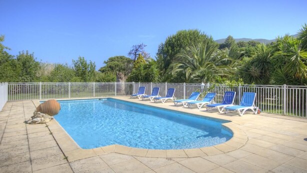 Une piscine rectangulaire à l’eau bleue, entourée d’une clôture blanche. Des chaises longues bleues sont alignées le long du bord de la piscine.