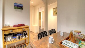 Een eetruimte met een houten tafel, stoelen, een koffiezetapparaat en een fles wijn.