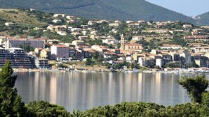 Un pueblo costero con edificios, una colina y una masa de agua tranquila.