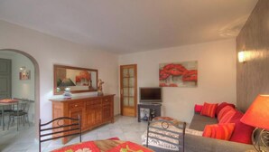 Una sala de estar con sofá, televisor, mueble y comedor con sillas y mesa.