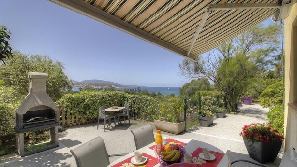 Un patio exterior con horno de piedra, asientos y una mesa lista para comer, con vistas a un paisaje pintoresco.