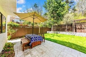 A patio with a table and chairs, a large umbrella, and a stone wall. - Bright Carmel Valley Home - 3BR, BIG YARD (San Diego)