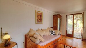 A room with a wooden sofa, a lamp, a painting, and a view through a glass door. - U PAGLIAGHJU - CATERI (CATERI)
