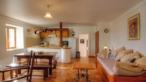 A cozy kitchen with wooden cabinets, a dining table with chairs, a built-in island, and a living area with a sofa and cushions. - U PAGLIAGHJU - CATERI (CATERI)