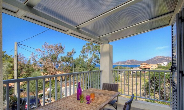 Un balcón con una mesa de madera, sillas y vista al mar y las montañas.