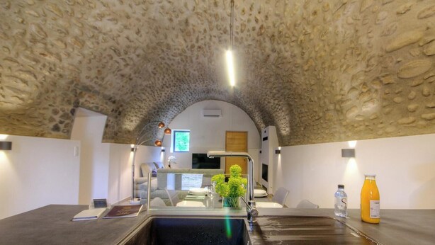 A kitchen with a stone ceiling, modern appliances, and a dining area with a table and chairs. - Casetta Anghjulina - CASTIFAO (CASTIFAO)