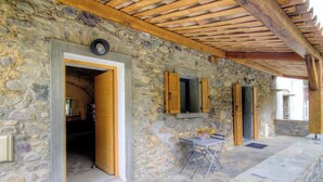 A stone building with a wooden ceiling, a table with chairs, and a window with shutters. - Casetta Anghjulina - CASTIFAO (CASTIFAO)