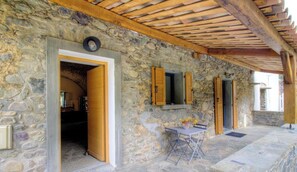 Ein Steinhaus mit Holzbalkendecke, einem Tisch mit Stühlen und einem Fenster mit Rollläden.