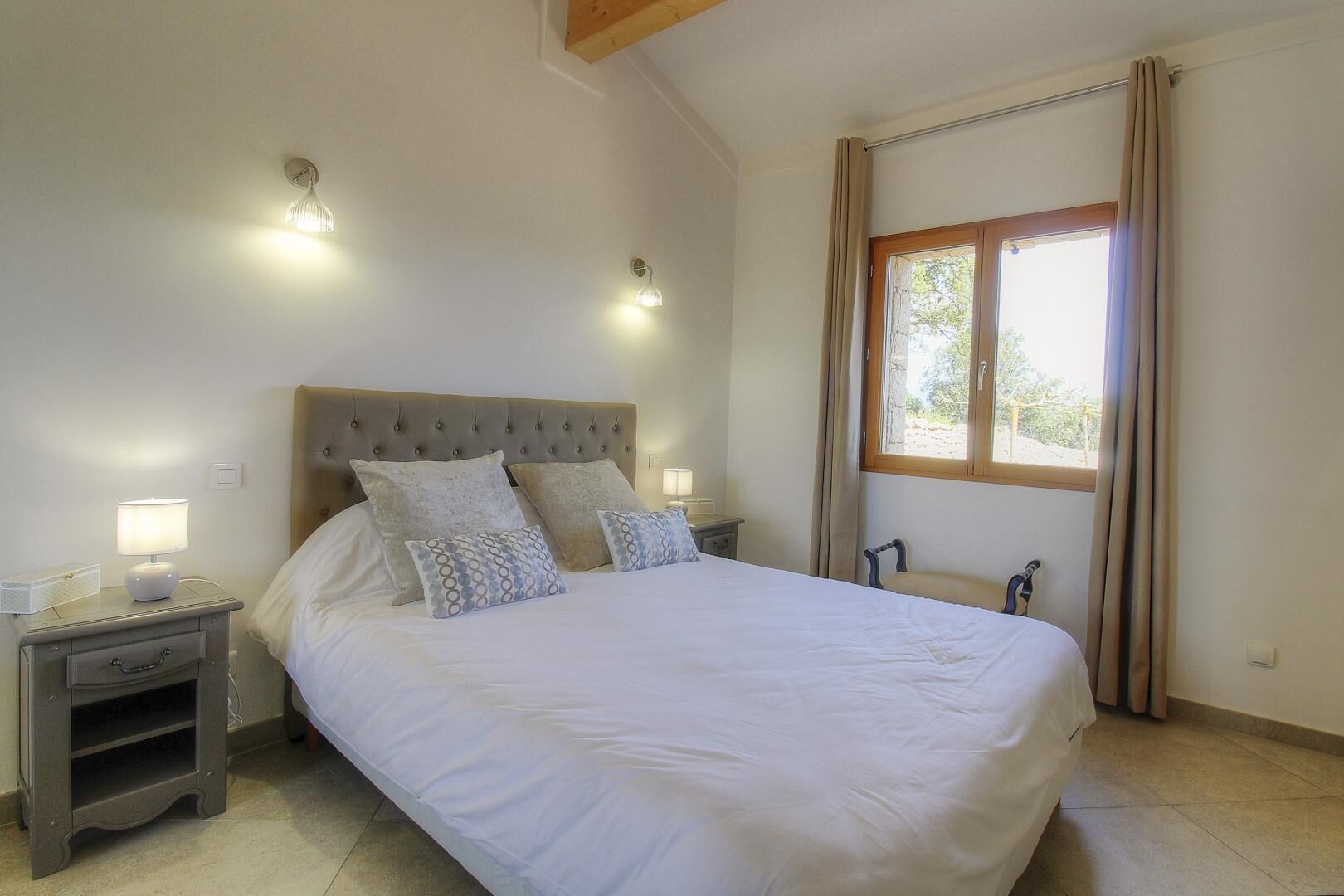 Une chambre à coucher avec un grand lit, deux lampes de chevet, une table de chevet, une fenêtre avec des rideaux et une poutre en bois au plafond.