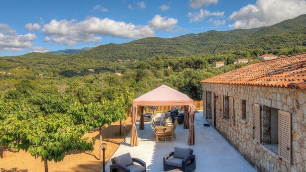 A villa with a terrace, outdoor seating, and a view of the surrounding hills.