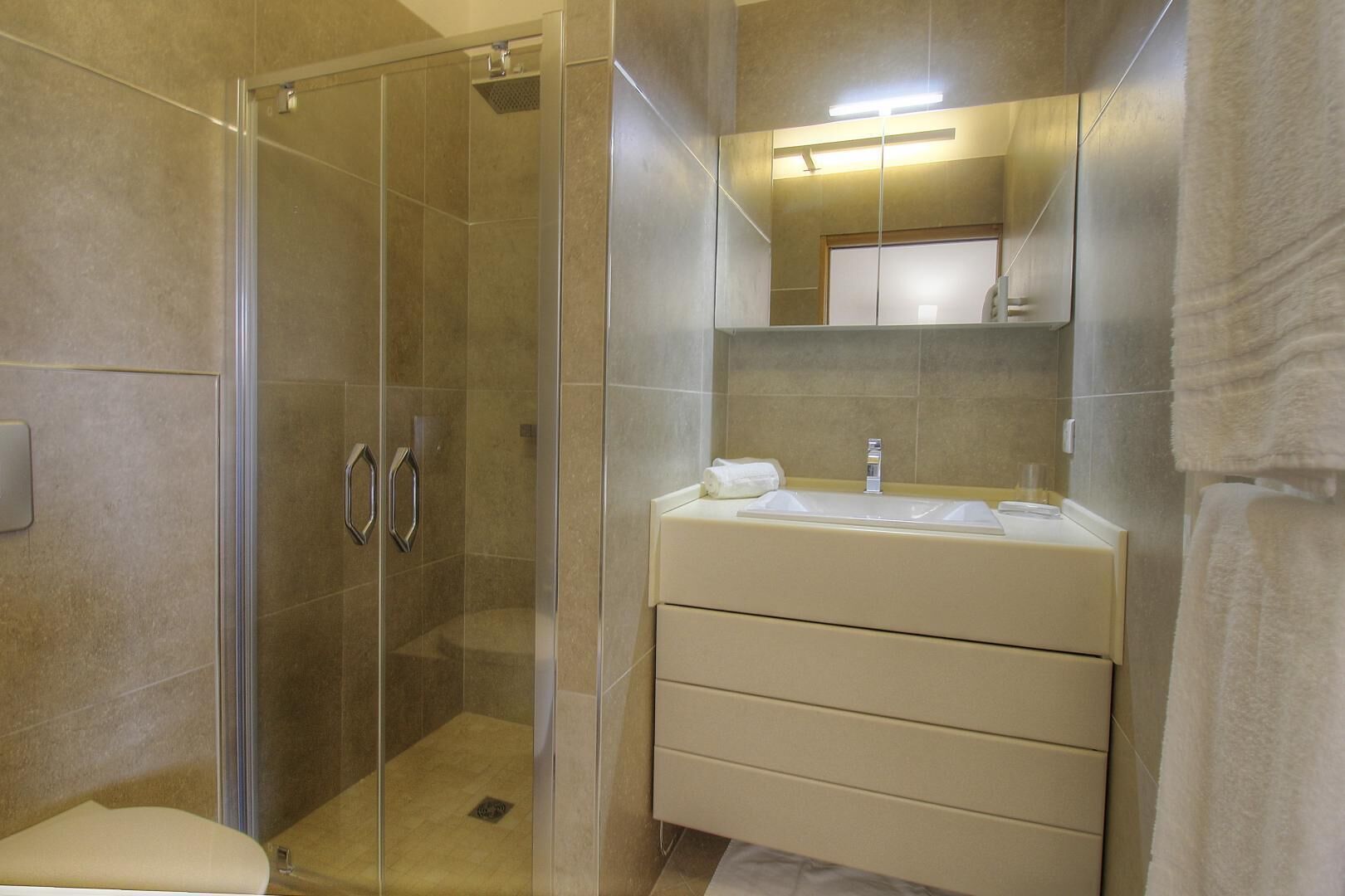 Une salle de bain moderne avec une douche à parois de verre, un meuble-lavabo beige avec un miroir et une serviette posée sur le plan de travail.