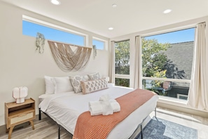 A bedroom with a large bed, a nightstand, a window with curtains, and a view of the outside.