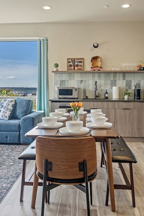 A modern kitchen with a dining area, a sofa, and a view of the city.