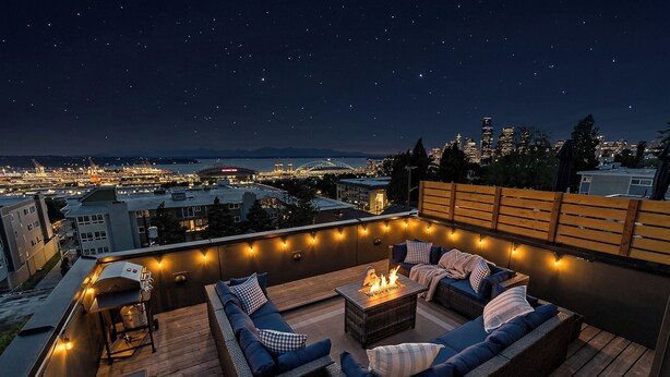 Terraza en la azotea con mobiliario exterior, una chimenea y luces colgantes.