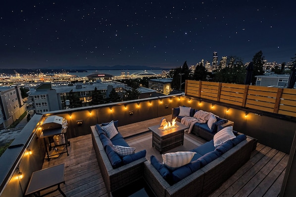 A rooftop patio with outdoor seating, a fire pit, and string lights.