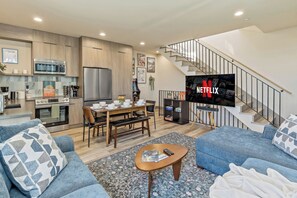 A modern living space with a kitchen, dining area, and a staircase leading to a loft.