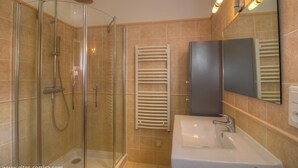 Una cabina doccia con pareti in vetro, un lavandino bianco con uno specchio sopra e un porta asciugamani con asciugamani bianchi.