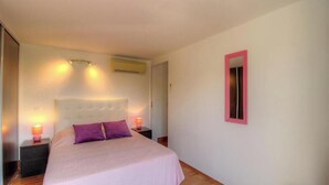 Une chambre à coucher comprenant un lit, des tables de chevet, un climatiseur fixé au mur et un miroir.